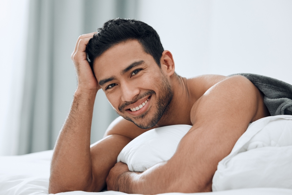 Young man lying in bed smiling and looking rested representing overall male health and wellbeing as it relates to understanding TRT and fertility before starting testosterone therapy