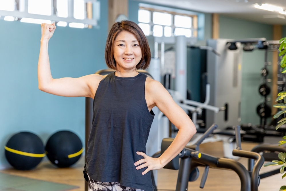 Middle-aged woman flexing her arm confidently in a gym representing the role of strength training in supporting weight loss after 40
