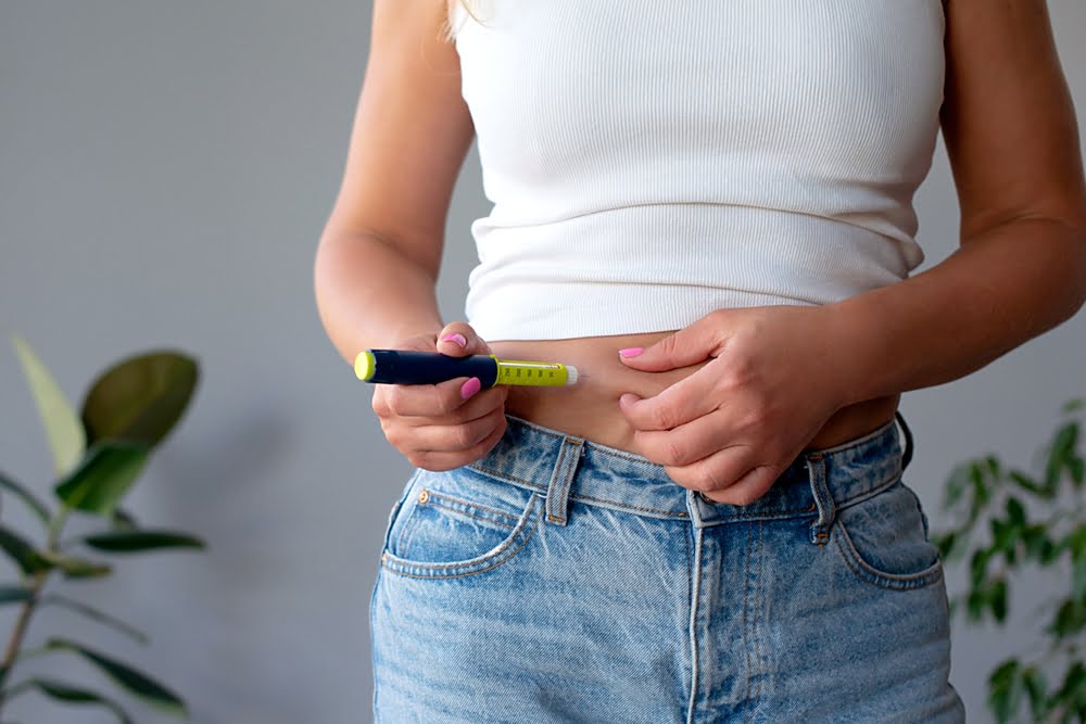 Woman self-administering a subcutaneous injection pen into her abdomen representing the GLP-1 medication component of combining medical weight loss with hormone therapy for improved metabolic outcomes