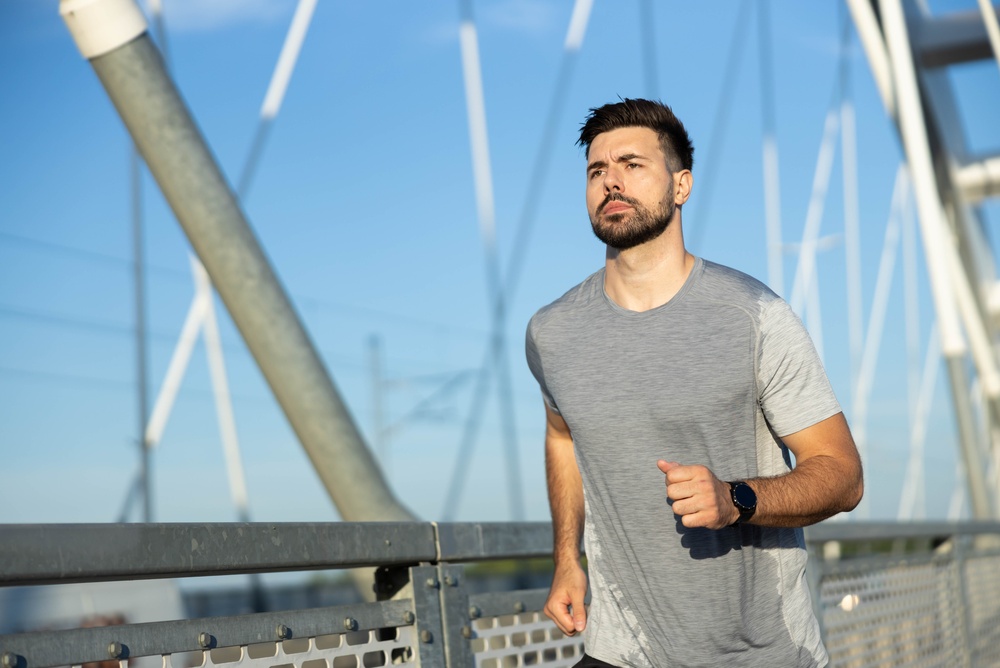 Focused man running outdoors on a bridge wearing a smartwatch representing the cardiovascular and physical activity lifestyle changes with TRT that improve testosterone therapy outcomes