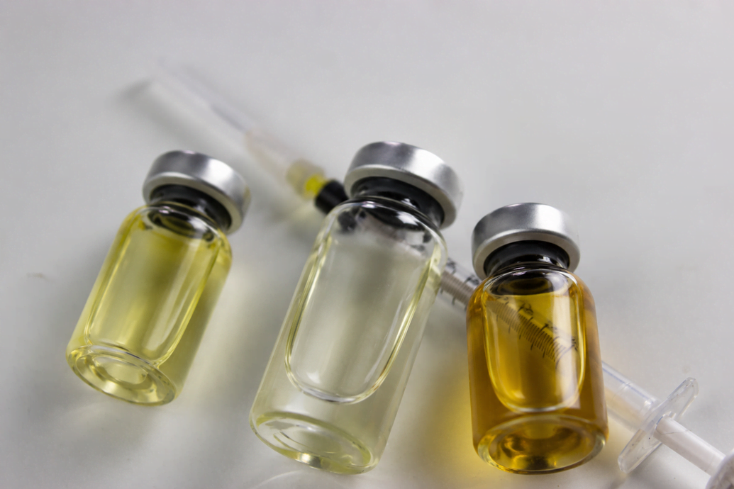 Three glass injectable vials with syringes on a white surface representing the clinical compounds used in TRT vs anabolic steroids and how medically prescribed testosterone differs from performance steroid use