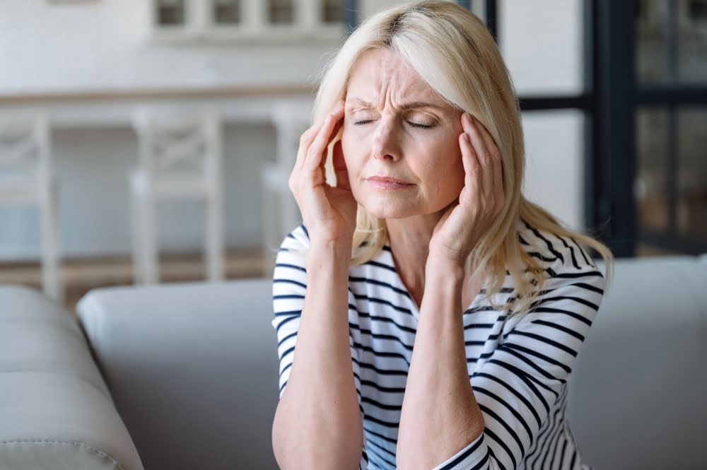 Middle-aged woman pressing her hands to her temples with eyes closed representing hormonal headaches and discomfort as common BHRT side effects during the early adjustment period of bioidentical hormone therapy