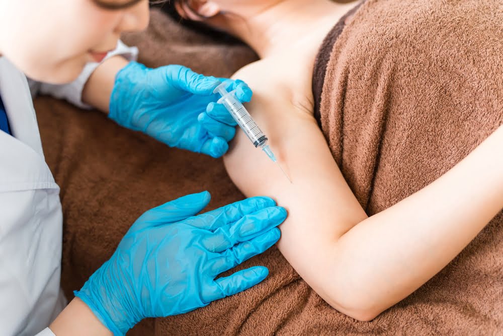 Gloved healthcare provider administering a subcutaneous injection into a patient's upper arm representing the clinical delivery method involved in combining peptide therapy with hormone treatment