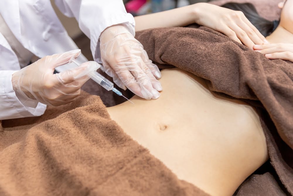Gloved healthcare provider administering a subcutaneous abdominal injection to a patient on a treatment table representing the clinical peptide therapy administration process and what patients can expect during treatment